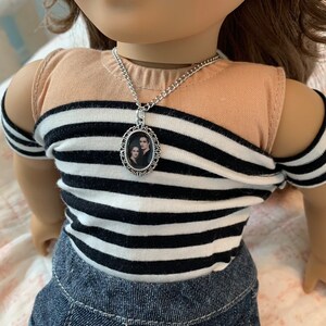 K&ouml;nnte beinhalten: Eine silberne Kettenkette mit einem ovalen Anh&auml;nger, der ein Schwarzwei&szlig;foto eines Paares zeigt. Die Kette wird von einer Puppe mit braunen Haaren und einem gestreiften Shirt getragen.