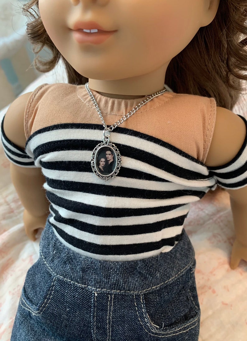 K&ouml;nnte beinhalten: Eine silberne Kettenkette mit einem ovalen Anh&auml;nger, der ein Schwarzwei&szlig;foto eines Paares zeigt. Die Kette wird von einer Puppe mit braunen Haaren und einem gestreiften Shirt getragen.