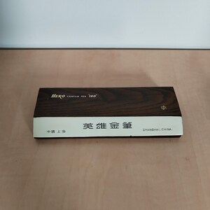 May include: A rectangular box with a dark wood grain finish and a white band. The text "HERO FOUNTAIN PEN '100'" is printed on the top. The box also has Chinese characters and the text "SHANGHAI, CHINA."