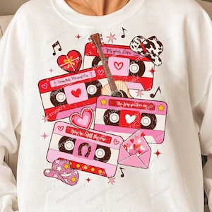 Può includere: Felpa bianca con una grafica di musicassette rosa e rosse, cuori, una chitarra e un cappello da cowboy. Il testo sui nastri recita "You're Still The One", "It's Your Love" e "The Day You Say I Love You".