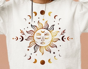 May include: A white sweatshirt with a gold sun and moon design. The sun has a face and is surrounded by stars and crescent moons.