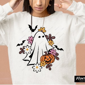 Pu&ograve; includere: Un fantasma bianco con un viso amichevole circondato da fiori arancioni, rosa e gialli e pipistrelli. Il fantasma tiene una zucca intagliata a forma di zucca.