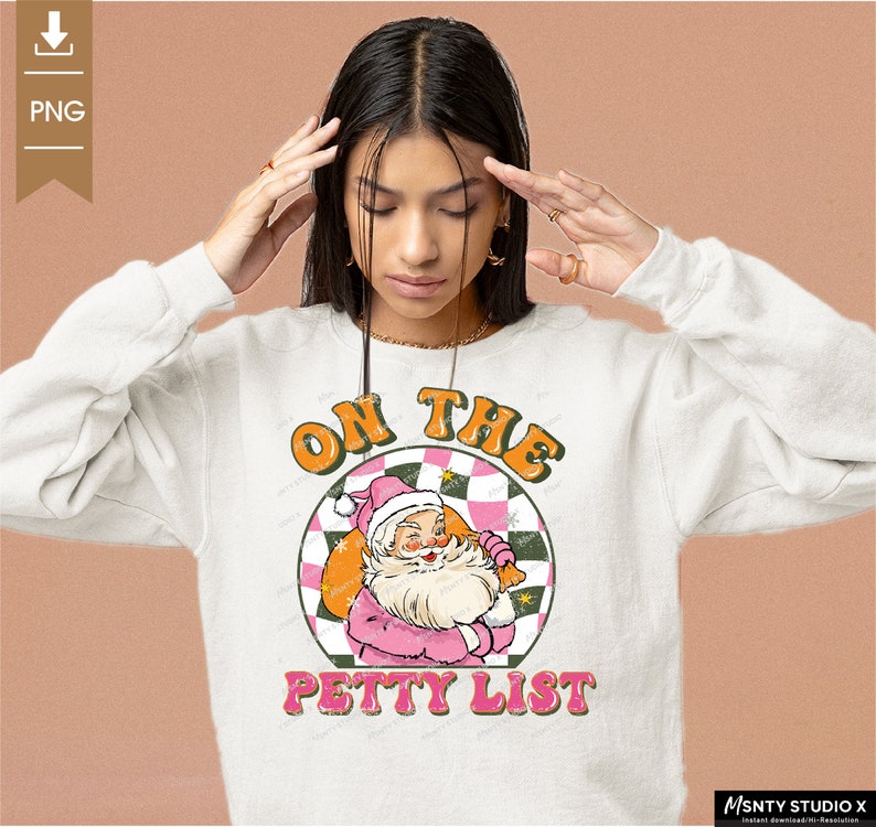 May include: A white sweatshirt with a pink and green graphic design featuring a cartoon Santa Claus holding a bag of gifts. The graphic text reads "On the Petty List".