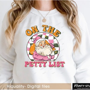 May include: A white sweatshirt with a pink and orange graphic design featuring Santa Claus with a bag of gifts. The graphic says "On the Petty List".