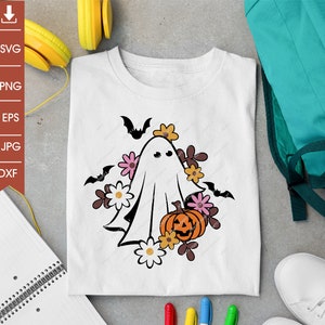 Pu&ograve; includere: Un fantasma bianco con un viso amichevole che tiene una zucca intagliata a forma di viso. Il fantasma &egrave; circondato da foglie marroni e fiori rosa e bianchi. Il design &egrave; su una maglietta bianca.