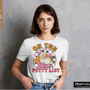 May include: White t-shirt with a vintage-style graphic of Santa Claus on a checkered background. The text "On the Petty List" is printed below the graphic.
