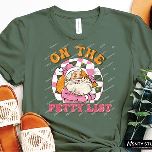 May include: A green t-shirt with a retro-style graphic of Santa Claus in a pink suit. The graphic says "On the Petty List" in a colorful, vintage font.