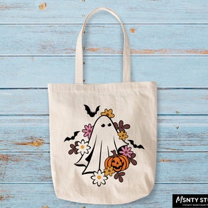 Pu&ograve; includere: Una borsa di tela bianca con un fantasma, una zucca e fiori stampati su di essa. Il fantasma ha un viso amichevole ed &egrave; circondato da pipistrelli e fiori. La zucca &egrave; arancione e ha un viso intagliato. I fiori sono rosa, gialli e marroni.