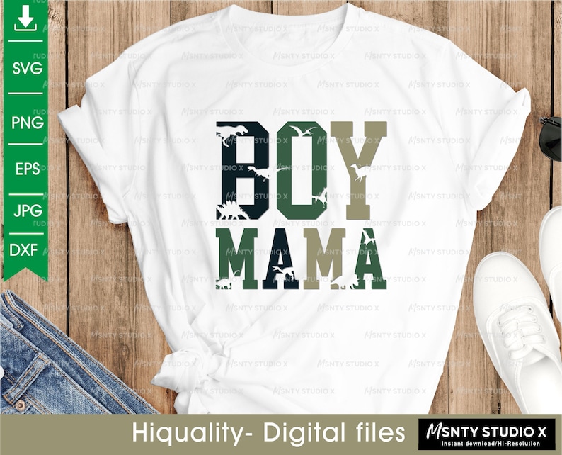 Pu&ograve; includere: Maglietta bianca con un design grafico verde, nero e beige che dice "BOY MAMA" con silhouette di dinosauri.