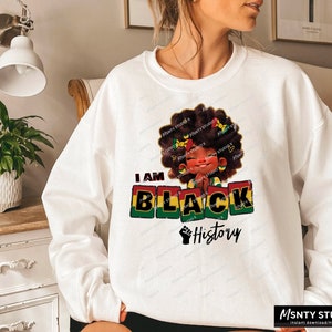 K&ouml;nnte beinhalten: Wei&szlig;es Sweatshirt mit einem Grafikdesign eines schwarzen M&auml;dchens mit Afro, das ein gr&uuml;n-gelb-rotes Stirnband tr&auml;gt. Der Text "I AM BLACK History" ist in roten, gelben und gr&uuml;nen Bl&ouml;cken gedruckt.