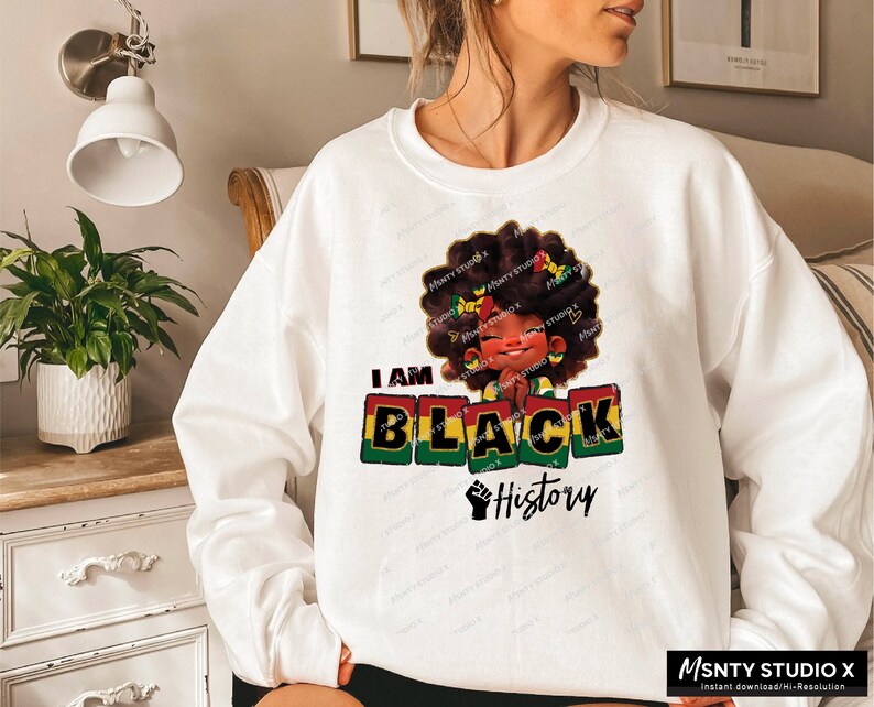K&ouml;nnte beinhalten: Wei&szlig;es Sweatshirt mit einem Grafikdesign eines schwarzen M&auml;dchens mit Afro, das ein gr&uuml;n-gelb-rotes Stirnband tr&auml;gt. Der Text "I AM BLACK History" ist in roten, gelben und gr&uuml;nen Bl&ouml;cken gedruckt.