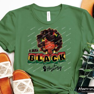 K&ouml;nnte beinhalten: Gr&uuml;nes T-Shirt mit einer schwarzen und braunen Illustration eines M&auml;dchens mit Afro und dem Text "I Am Black History".