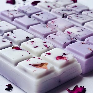 May include: Close-up of wax melts in a square shape, divided into rectangular sections. The wax is white and lavender, with dried rose petals sprinkled on top. The arrangement suggests a spa or aromatherapy product.