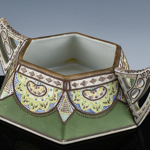 May include: A hexagonal ceramic dish with two ornate handles. The dish is decorated with a green, brown, and yellow geometric pattern.