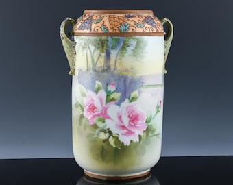 May include: A hand-painted ceramic vase featuring a landscape and pink roses. The vase has two handles and a decorative rim. The colours include pink, green, yellow, and brown.