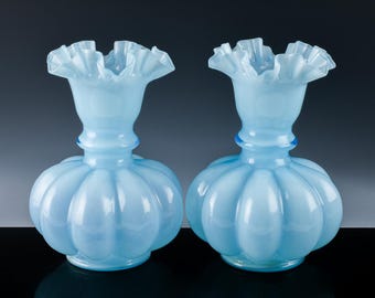 May include: Two light blue glass vases with ruffled tops and a textured, ribbed body. The vases are made of opalescent glass.