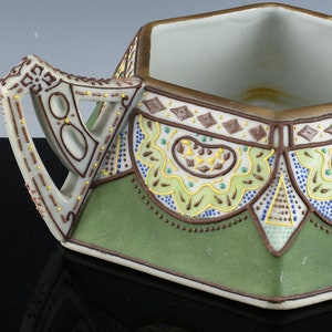 May include: A hexagonal ceramic sugar bowl with a green and brown geometric design. The bowl has a handle and a white interior.