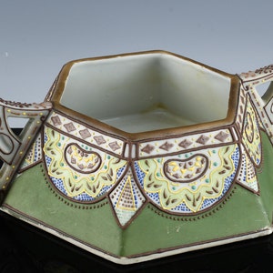 May include: A hexagonal ceramic sugar bowl with two handles. The bowl is decorated with a green, brown, yellow, and blue geometric pattern.