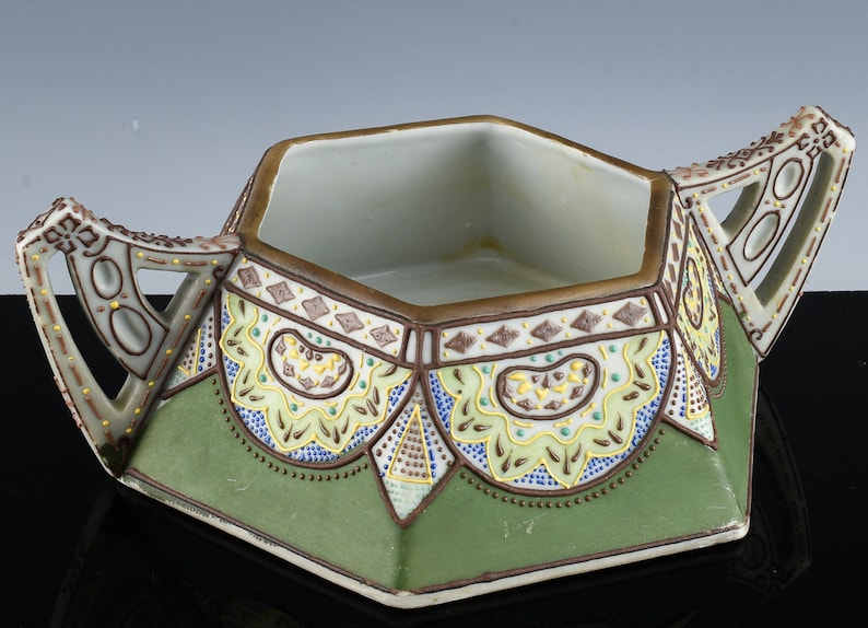 May include: A hexagonal ceramic sugar bowl with two handles. The bowl is decorated with a green, brown, yellow, and blue geometric pattern.