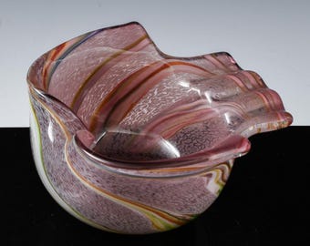 May include: A pink and white glass bowl with a wavy, organic shape and a swirl pattern. The bowl is made of clear glass with streaks of pink, white, and brown.
