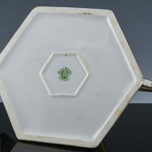 May include: The underside of a white hexagonal teapot with a green and white "Hand Painted Nippon" mark.