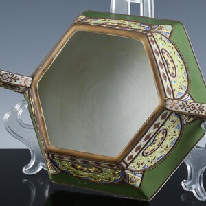 May include: A hexagonal ceramic bowl with two handles. The bowl is decorated with a green, brown, and gold floral pattern. The bowl is empty.