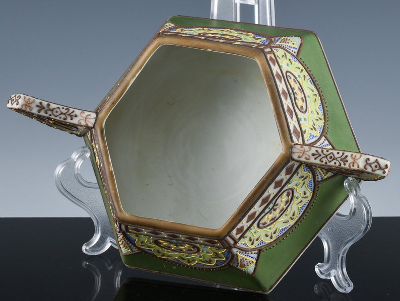 May include: A hexagonal ceramic bowl with two handles. The bowl is decorated with a green, brown, and gold floral pattern. The bowl is empty.
