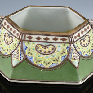 May include: Octagonal porcelain sugar bowl with green, brown, blue, and yellow floral and geometric patterns. The bowl has two handles and a gold rim.