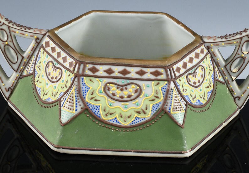 May include: Octagonal porcelain sugar bowl with green, brown, blue, and yellow floral and geometric patterns. The bowl has two handles and a gold rim.