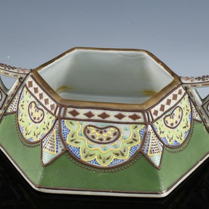 May include: Octagonal porcelain sugar bowl with two handles. The bowl is decorated with green, yellow and brown floral patterns and gold accents.