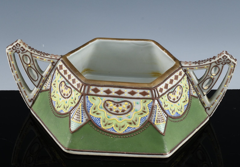 May include: Octagonal porcelain sugar bowl with two handles. The bowl is decorated with green, yellow and brown floral patterns and gold accents.
