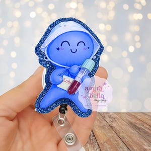 May include: A blue badge reel with a cartoon lab character holding a blood vial. The character is smiling and wearing a white hat. The badge reel has a glittery blue border and a clear plastic clip for attaching to clothing.