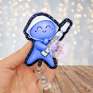 Puede incluir: Un portatarjetas azul con un personaje de dibujos animados que lleva una mascarilla quirúrgica y sostiene un vial con la etiqueta "Albuterol Sulfate Inhalation Solution Sterile". El portatarjetas tiene un borde azul oscuro brillante y un clip retráctil de plástico transparente.