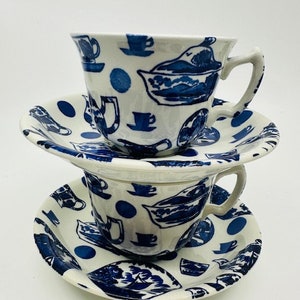 Puede incluir: Un juego de dos tazas de té y platillos azules y blancos con un patrón caprichoso de teteras, tazas y platillos. El patrón se repite tanto en las tazas como en los platillos.