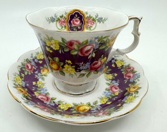 May include: A purple and white teacup and saucer set with a floral pattern. The cup and saucer have a gold trim.