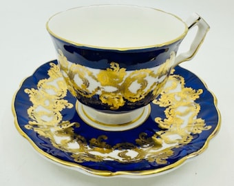 May include: A blue and gold teacup and saucer set with a delicate floral pattern. The cup and saucer are both trimmed in gold.