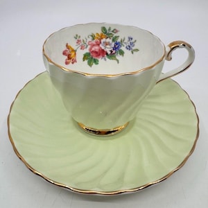 May include: A pale green teacup and saucer set with gold trim. The teacup has a floral design inside with pink, red, yellow, and blue flowers. The saucer has a spiral design. A classic vintage tea set for serving tea.
