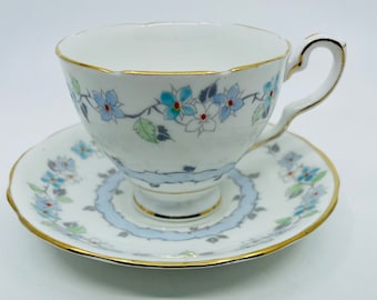 May include: A white teacup and saucer set with a blue and white floral pattern. The cup and saucer have a gold trim.