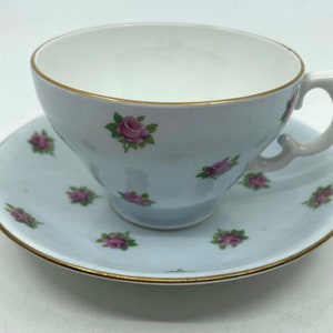 Peut inclure: Une tasse à thé et une soucoupe délicates avec un fond bleu clair et un motif de petites roses roses. L'ensemble est orné d'une bordure dorée.