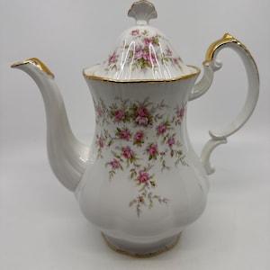 Peut inclure: Théière en porcelaine blanche avec couvercle, ornée de motifs floraux de roses roses et de bordures dorées. La théière présente un bec et une anse incurvés, et un bouton décoratif sur le couvercle. Une pièce classique pour servir le thé.