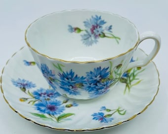 May include: A white teacup and saucer set with a blue and white floral pattern. The cup and saucer have a gold trim around the edges.