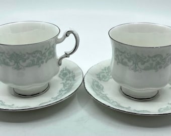 May include: Two white teacups and saucers with a delicate green floral pattern and silver trim.