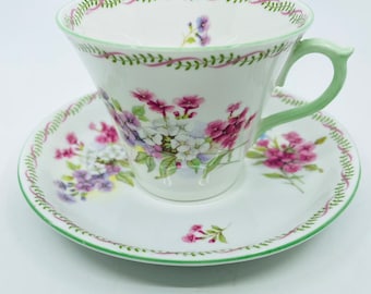 Puede incluir: Un juego de taza y platillo de té blanco con un patrón floral. La taza y el platillo tienen un borde verde y rosa.