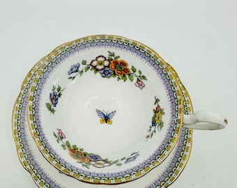 May include: A white teacup and saucer with a floral pattern in shades of pink, yellow, blue, and green. The cup and saucer have a gold trim and a delicate butterfly design.
