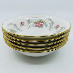 Puede incluir: Un conjunto de cinco cuencos de porcelana blanca con un borde dorado y un patrón floral. Los cuencos están apilados sobre una superficie blanca.