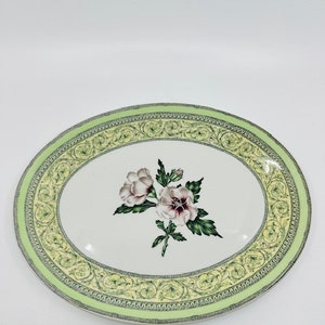 Può includere: Un piatto da portata ovale bianco con un bordo floreale verde e giallo. Il centro del piatto presenta un motivo floreale rosa e bianco con foglie verdi.