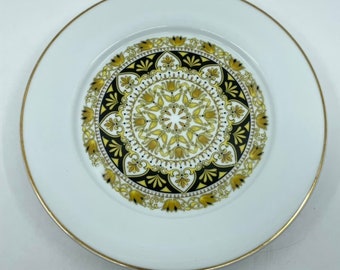 May include: White ceramic dinner plate with a gold rim and a black and gold geometric design in the center.