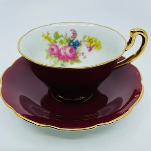 Può includere: Un set da tè in porcellana color borgogna con bordo dorato e un motivo floreale all'interno della tazza.