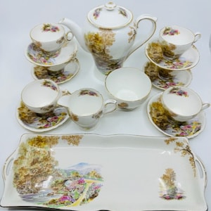 May include: A vintage tea set with a floral pattern. The set includes a teapot, creamer, sugar bowl, and six teacups and saucers. The set is decorated with a floral pattern and a landscape scene. The set is also accompanied by a matching serving tray.