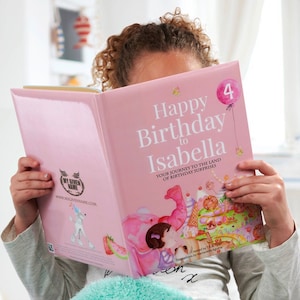 Pode incluir: Um livro personalizado rosa com o texto "Happy Birthday to Isabella" e um bal&atilde;o rosa com o n&uacute;mero 4. O livro est&aacute; aberto em uma p&aacute;gina com uma ilustra&ccedil;&atilde;o de uma menina com um vestido rosa e um elefante rosa.